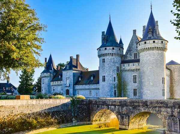 Vue du Château de Sully-sur-Loire avec ses tours médiévales et son pont de pierre au-dessus des douves, illuminé par le soleil levant.