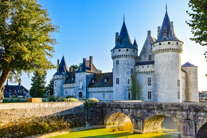 Vue du Château de Sully-sur-Loire avec ses tours médiévales et son pont de pierre au-dessus des douves, illuminé par le soleil levant.